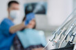© JJ Studio - dental tools with dentist and patient on background.