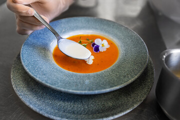 food cooking, profession and people concept - close up of chef serving plate of pumpkin cream soup and adding cream at restaurant kitchen