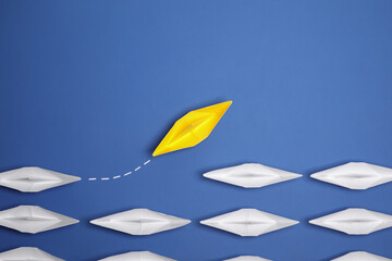 Sticker - Yellow paper boat floating away from others on blue background, flat lay with space for text. Uniqueness concept