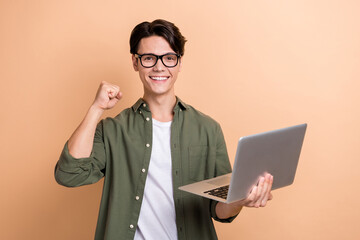 Poster - Photo of positive man use wireless netbook raise fist celebrate triumph isolated on beige color background