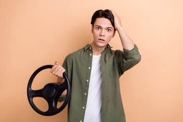 Poster - Photo of dissatisfied guy with brunet hair dressed khaki shirt hold steering wheel palm on head isolated on beige color background