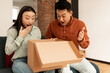 © Prostock-studio - Happy surprised asian couple unpacking cardboard box with delivered items, sitting on sofa at home