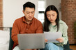 © Prostock-studio - Upset korean spouses checking bills, reading documents while sitting on couch and using laptop. Family budget concept