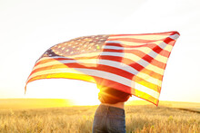 Woman In Field Holding USA Stars And Stripes Flag In Golden Sunset Evening Sunshine