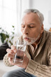 © LIGHTFIELD STUDIOS - grey haired man with parkinsonism holding glass of water in trembling hands at home.