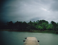 An Old Wooden Fishing Dock Leads To The Water As An Approaching Summer Storm Threatens A Lake.