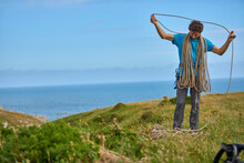 Full Length Shot Of A Male Rock Climber Coiling Rope On Seashore, Pembroke, Wales, UK