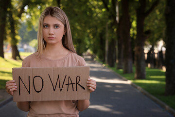 Wall Mural - Sad woman holding poster with words No War in park. Space for text