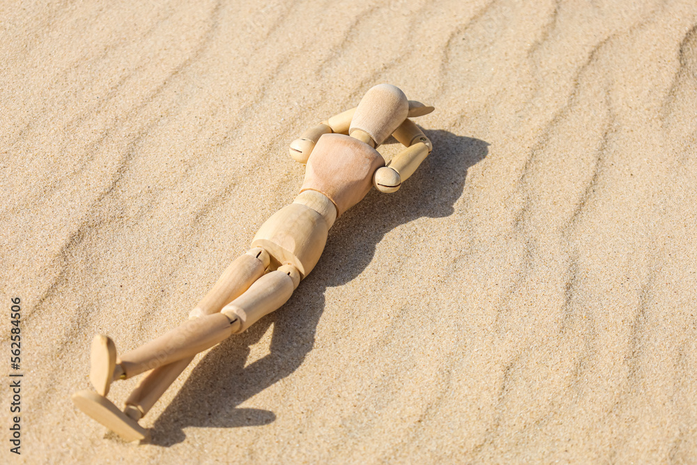Wooden mannequin lying on sand