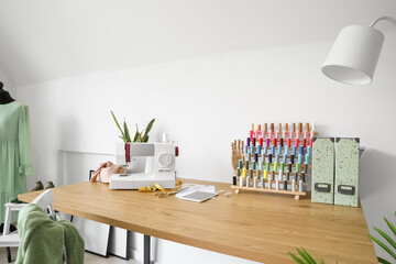 Poster - Tailor's workplace with sewing machine and thread pools near light wall in atelier