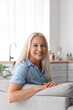 © Pixel-Shot - Mature woman sitting on sofa in kitchen