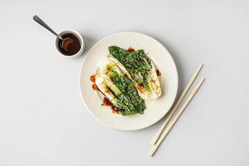 Plate of tasty stewed pak choi cabbage with soy sauce and chopsticks on white background