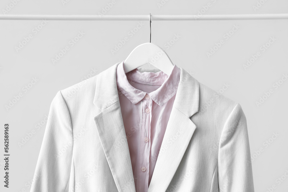 Rack with female jacket and shirt near light wall, closeup
