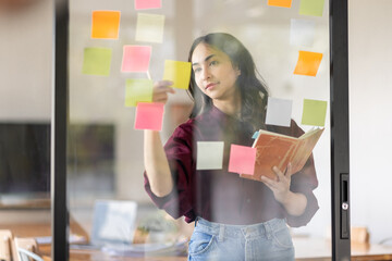 Business female employee with many conflicting priorities arranging sticky notes commenting and brainstorming on work priorities colleague in a modern office.
