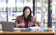 © David - Freelancer Happy business Asian woman in knitwear taking notes at laptop sitting at desk office, finance concept.
