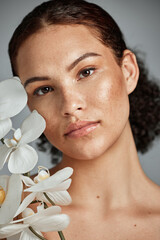 Wall Mural - Face portrait, skincare and woman with orchid in studio isolated on a gray background. Floral makeup, organic cosmetics and female model with flowers for healthy skin treatment, wellness and beauty