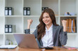 © amnaj - Attractive Asian woman happy at plan success with happy smile on computer laptop and document.