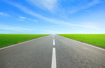 Wall Mural - strait tarmac road in grass field with blue sky background.