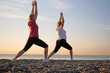 Two women doing yoga performing asanas and enjoying life on the beach sea, sunset time