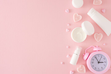 Women skin care concept. Flat lay photo of cosmetic bottles, cream jars, heart shaped candles and alarm clock on pastel pink background with copy space. Mother's day Or Valentines idea