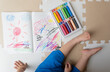 A boy is drawing with crayons on a sketchbook