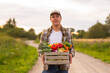 © Acronym - Farmer with a vegetable box in front of a sunset agricultural landscape. Man in a countryside field. Country life, food production, farming and country lifestyle concept.