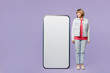 © ViDi Studio - Full body happy elderly blonde woman 50s years old wear casual clothes denim jacket t-shirt look at big huge blank screen mobile cell phone with area isolated on plain pastel light purple background.