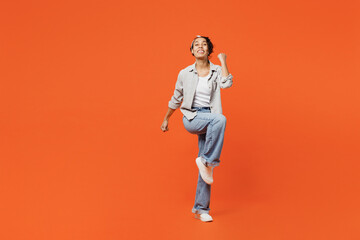 Poster - Full body young woman of African American ethnicity she wears grey shirt headband doing winner gesture celebrate clenching fists say yes isolated on plain orange background. People lifestyle concept.