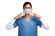 © peopleimages.com - Portrait of a young doctor pointing to her surgical face mask Isolated on a PNG background.