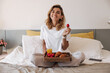 © Look! - Happy young caucasian woman sitting on bed with strawberries and breakfast tray indoor. Girl wears pajamas looking at camera wide smile. Concept healthy morning