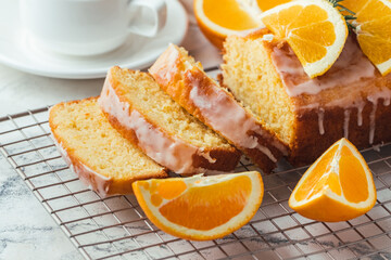 Wall Mural - Loaf of orange bread covered with a confectionery glaze with lemon juice and decorated with orange slices. Chiffon cake on a pastry grill next to cup of tea. White background