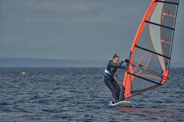 Mature woman beginner windsurfer moves slowly on a sailboard on a sunny autumn day.