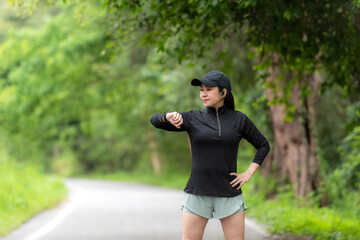 Wall Mural - Healthy  woman relax after cool down and looking smart watch for check timing run.  Asian runner woman workout after fitness and jogging session at the park. Healthy and Lifestyle Concept