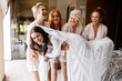 Front view of crazy and pretty maids of honor with perfect hairdo and makeup, wearing in stylish peignoirs, standing and keeping bride, which lying on their hands, smiling and having fun