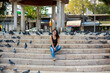 A beautiful girl is sitting on the steps in the park surrounded by pigeons
