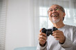 © sorapop - Funny retirement elderly smile sitting on sofa life gaming, lifestyle senior old man enjoying holding joystick playing video game at home, gamer mature man hands using game controller play videogame