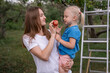 © somemeans - Young mother treats blonde daughter to ripe red apple . Mom and child harvest apples in garden