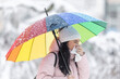 Woman with an umbrella outdoors sneezes into a napkin, getting cold from the bad winter weather
