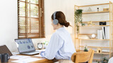 Fototapeta  - Asian female college student wearing headphones watching live performance or video call teacher teaching on laptop, Conversations with teachers and classmates, Online learning, Study at your own home.