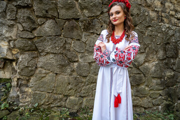 Wall Mural - Portrait of a beautiful Slavic girl with long blond hair and blue eyes with a flower crown in a white and red embroidered dress with a bouquet. Traditional clothes of the Ukrainian