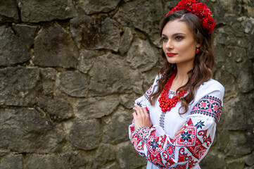 Wall Mural - Portrait of a beautiful Slavic girl with long blond hair and blue eyes with a flower crown in a white and red embroidered dress with a bouquet. Traditional clothes of the Ukrainian