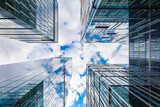Fototapeta  - Look up to high skyscrapers corporate buildings with glass walls and reflecting beautiful cloudy sunny sky
