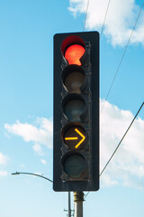 Red color and yellow arrow on the traffic light with cloudy sky on the background