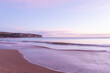 Sublime colours of sunrise over calm beach with cliffs in background