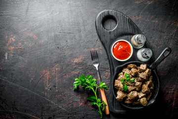 Sticker - Fried liver in a frying pan on a cutting Board with parsley, sauce and spices.