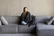 © F8  \ Suport Ukraine - Cutewoman relaxing o the sofa wrapped in a soft grey blanket