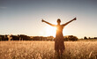 Having a positive mindset, wellbeing and hope concept. Happy young woman standing in a nature sunrise field with arms outstretched. 