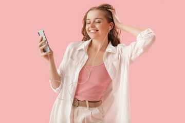 Wall Mural - Young woman in earphones with mobile phone listening to music on pink background