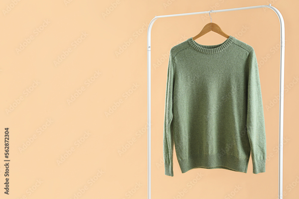 Rack with green sweater on beige background