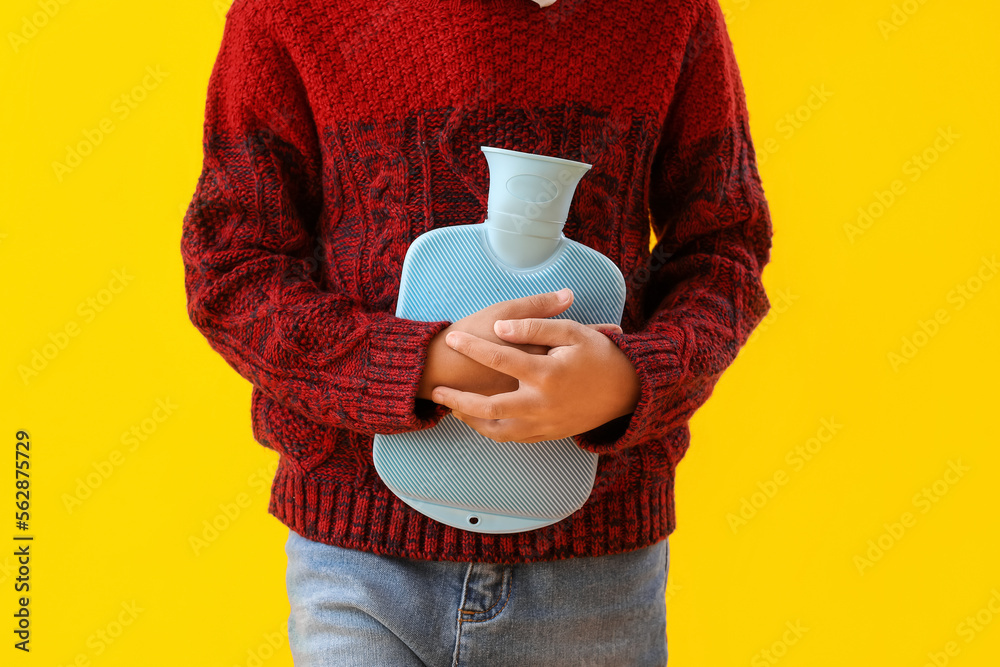 Ill boy with hot water bottle on yellow background, closeup